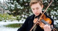 Young male violinist performing outdoors in winter snow, classical musician playing wooden violin with bow in snowy park setting for concert promotion.