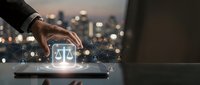 Businessman hand touching digital tablet with glowing justice scales icon and network connections against blurred city lights background at night.
