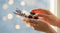 Female hands holding aromatic winter spices including star anise and lavender with magical bokeh lights and sparkles creating cozy seasonal atmosphere.