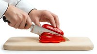 Chef's hands slicing fresh red bell pepper on wooden cutting board with sharp knife, isolated on white background for culinary content.