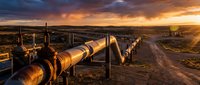 Industrial oil pipeline infrastructure stretching across desert landscape during golden hour sunset with dramatic cloudy sky and construction equipment.