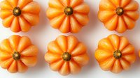 Bright orange decorative mini pumpkins arranged in neat rows on white background. Seasonal autumn gourds with ribbed texture and stems create symmetrical pattern.