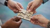 Business teamwork concept with hands connecting wooden puzzle pieces labeled mission, vision, strategy and execution against blurred background.