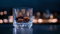 Crystal glass with dried dates on dark background with blurred city lights bokeh, moody atmospheric food photography for luxury dining and Ramadan concept.