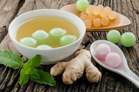 Fresh ginger tea with colorful candy balls and mint leaves on rustic wooden table. Herbal beverage with sweet treats for wellness and relaxation.