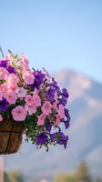 Hanging basket filled with vibrant pink and purple petunias blooming against soft blue sky with fluffy clouds for spring garden decoration.