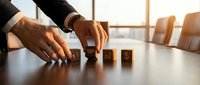 Professional businessman arranging wooden blocks spelling GOAL on conference table in modern office boardroom during strategic planning session.