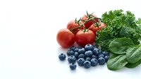 Fresh organic vegetables and berries on white background with tomatoes, blueberries, kale and spinach leaves for healthy cooking and nutrition concepts.