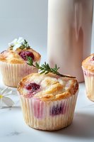 Fresh raspberry muffins with rosemary garnish on marble surface, soft natural lighting creates appetizing mood for bakery and cafe marketing.