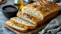 Freshly baked artisan bread loaf with mixed seeds on wooden cutting board, sliced and ready to serve for breakfast or dinner meal preparation.