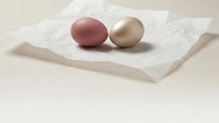 Two colored eggs in burgundy and gold tones placed on white marble surface with soft natural lighting for Easter celebration and spring decoration.