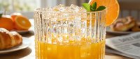 Refreshing orange juice cocktail in crystal glass with ice, mint garnish, and citrus slice, served at a sunny breakfast table.