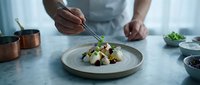 Chef plating gourmet salad with fresh vegetables and greens on white ceramic dish in modern kitchen setting for culinary, restaurant, and food service design projects.