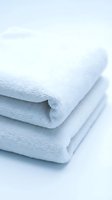 Stack of soft white folded terry towels on light background, conveying cleanliness and luxury for spa, hotel, and bathroom concepts.
