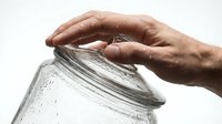 Senior hands carefully opening glass jar with condensation drops on white background for kitchen and cooking concepts.