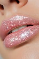 Close up of glossy pink lips with sparkly glitter makeup, showing white teeth. Macro beauty shot highlighting professional cosmetics application and glamorous shine.