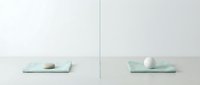 Minimalist composition with two pale green rectangular trays separated by vertical line, each holding single sphere, one beige and one white, on neutral background for design and branding projects.