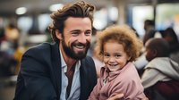 Caucasian bearded businessman in suit jacket sharing joyful moment with mixed race curly-haired toddler girl in pink hoodie, expressing genuine happiness and connection.