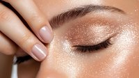 Glamorous close up of woman's eye with shimmering rose gold eyeshadow, long eyelashes and nude manicure showing modern beauty and makeup trends.