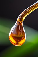 Golden honey drop falling in macro shot against blurred green background, showcasing viscosity and amber color in natural lighting.