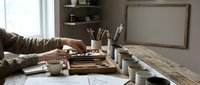 Artist workspace with paintbrushes, palette, and art supplies on wooden table near window. Creative studio setup for painting and drawing projects.