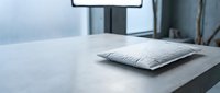 White sealed silica gel desiccant packet on gray concrete surface in industrial setting, moisture absorber for packaging and storage protection.