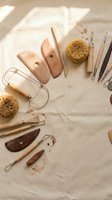 Pottery tools arranged in a semicircle on linen fabric, including wooden ribs, wire cutters, sponges, and sculpting tools for ceramic art.