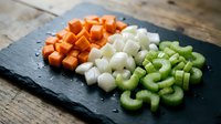Fresh diced vegetables on slate board including orange carrots, white onions and green celery ready for cooking and meal preparation.