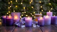 Purple candles burning with amethyst crystals on wooden surface with warm fairy lights creating peaceful meditation and wellness atmosphere.