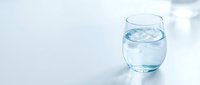 Glass of fresh water with ice cubes on white surface, suitable for health, wellness, hydration, and beverage advertising concepts.