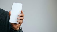 Close-up of a man's hand holding a blank white smartphone with empty screen against neutral background for app mockup or mobile technology concept.