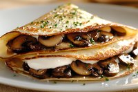Savory crepes filled with sauteed mushrooms, melted mozzarella cheese and fresh herbs served on white plate, close up view of French cuisine delicacy.