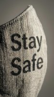 Fabric face mask with Stay Safe text printed on linen textile surface, close-up shot for health awareness and safety campaigns.
