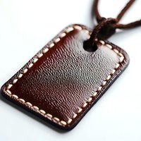 Brown leather tag with decorative stitching along edges on white background, close-up macro shot showing detailed grain texture and craftsmanship.