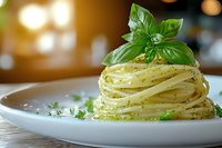 Coiled spaghetti pasta nest with pesto sauce and fresh basil leaves on white plate, garnished with herbs against warm bokeh background, macro food photography.