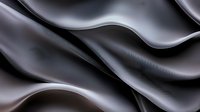 Elegant flowing waves of black and silver silk fabric create dramatic light and shadow effects, showcasing luxurious textile movement and abstract artistic curves.