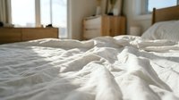 Unmade bed with white rumpled sheets and wooden furniture in bright sunlit bedroom interior, suitable for home decor, lifestyle, and hospitality design projects.