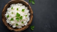 Cooked white rice garnished with fresh parsley in wooden bowl on dark slate background for healthy meal preparation and cooking concepts.