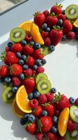 Fresh mixed berries and citrus fruits arranged on white plate in natural sunlight for healthy eating and nutrition concepts.