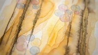 Abstract watercolor painting with flowing golden yellow brushstrokes and soft purple circles on textured paper background for creative projects.
