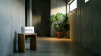 Minimalist concrete hallway with a wooden bench, welcome sign, and monstera plant in warm natural light, evoking modern interior design.