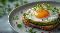 Fried egg on whole grain toast with avocado slices, fresh microgreens, and pink peppercorns on gray plate. Healthy breakfast or brunch option.