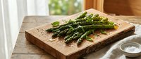 Fresh green asparagus with basil leaves and black pepper on a rustic wooden cutting board, natural light, healthy cooking concept.