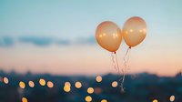 Peach-colored balloons floating against sunset sky with blurred bokeh lights creating dreamy atmosphere. Romantic celebration moment captured at dusk.