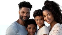 Happy African American family portrait with parents and two children smiling together on white background for lifestyle and parenting concepts.