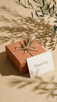Terracotta gift box tied with twine and olive branch beside a thank you card, warm beige background with natural leaf shadows.