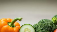 Fresh organic vegetables including orange bell pepper, cucumber slices and green broccoli arranged on neutral background for healthy cooking concepts.