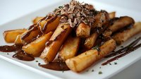 Golden french fries topped with rich chocolate sauce and shaved chocolate pieces served on white plate, creating sweet and savory fusion dessert combination.