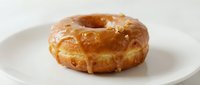 Glazed donut with golden-brown fried exterior on white plate, suitable for bakery, food, and culinary content.