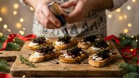 Woman preparing festive holiday appetizers with cranberry sauce on wooden board surrounded by Christmas decorations and warm bokeh lights for entertaining.